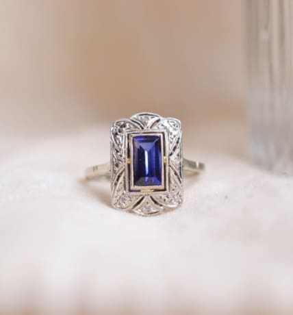 Bague style Art Déco rectangulaire en Or blanc 18 carats et Platine ornée d'un Saphir Verneuil taille à degrés dans un entourage stylisé ponctué de roses de Diamants