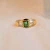 Bague ancienne en Or jaune 18 carats centrée d'une Émeraude sertie clos épaulée de baguettes de Diamants