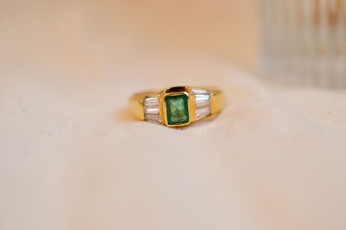 Bague ancienne en Or jaune 18 carats centrée d'une Émeraude sertie clos épaulée de baguettes de Diamants