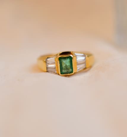 Bague ancienne en Or jaune 18 carats centrée d'une Émeraude sertie clos épaulée de baguettes de Diamants