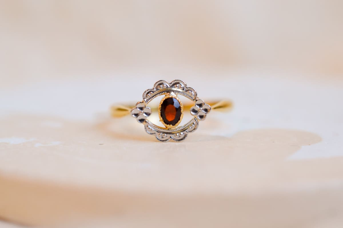 Bague ancienne en Or jaune 18 carats centrée d'un Grenat serti clos sur une table en fleurettes ajourée en Or blanc