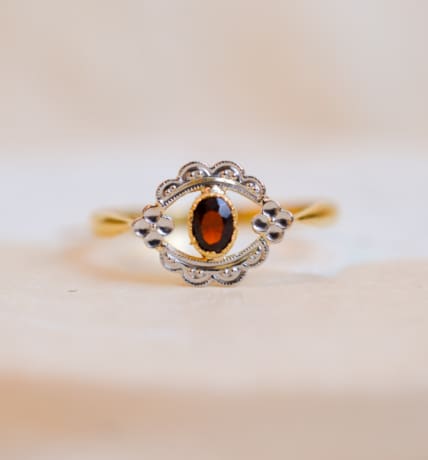 Bague ancienne en Or jaune 18 carats centrée d'un Grenat serti clos sur une table en fleurettes ajourée en Or blanc