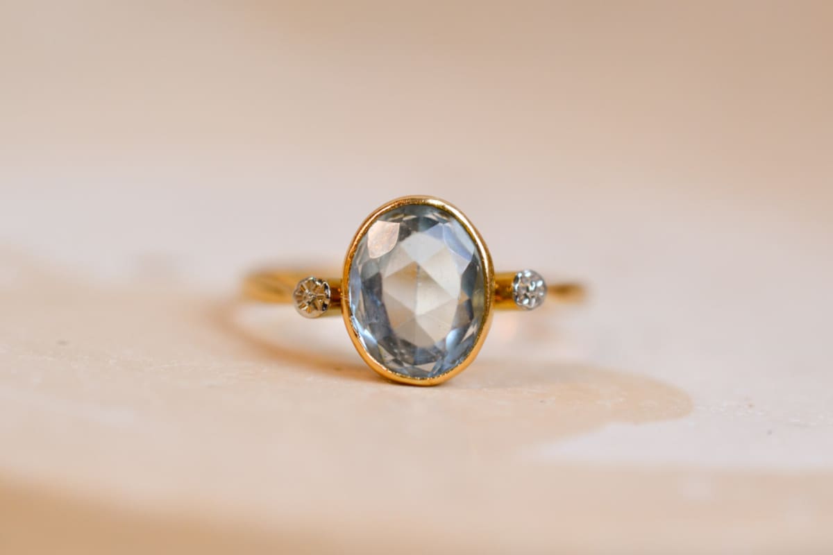 Bague ancienne en Or jaune 18 carats centrée d'une Aigue-Marine sertie clos épaulée par des fleurs d'Or blanc